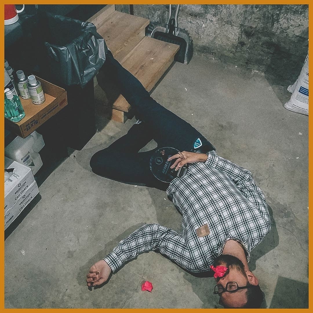 Everything in the frame is a clue—or a red herring. Of note: coffee cup (upper left corner), pink sticky notes, the chocolate smear on the award, the beard comb protruding from Adam's shirt pocket and the Ice Breakers gum container sticking out of his jeans.